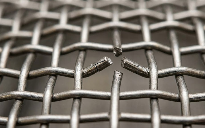 Macro detail of broken stainless steel wire mesh showing mechanical fatigue and micro-cracks